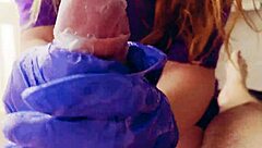 in a quiet room, a redhead works a huge cock with gloved hands, ending in a cum-covered mess.