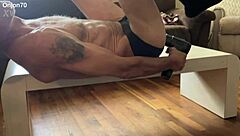 The bodybuilder lies on the desk for an aggressive myofascial pressure and release stretching session in underwear using a percussion massager